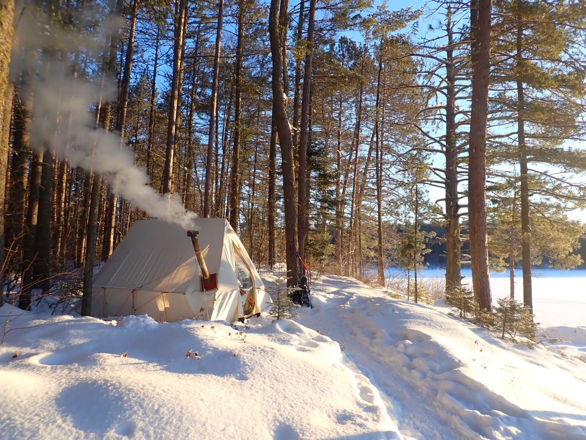 Earlier winter shelter: canvas tent, stove pipe, snow, and a setup made for weather already known. A reminder that winter comfort comes less from gentleness than from preparation and a shelter that has already been tested.