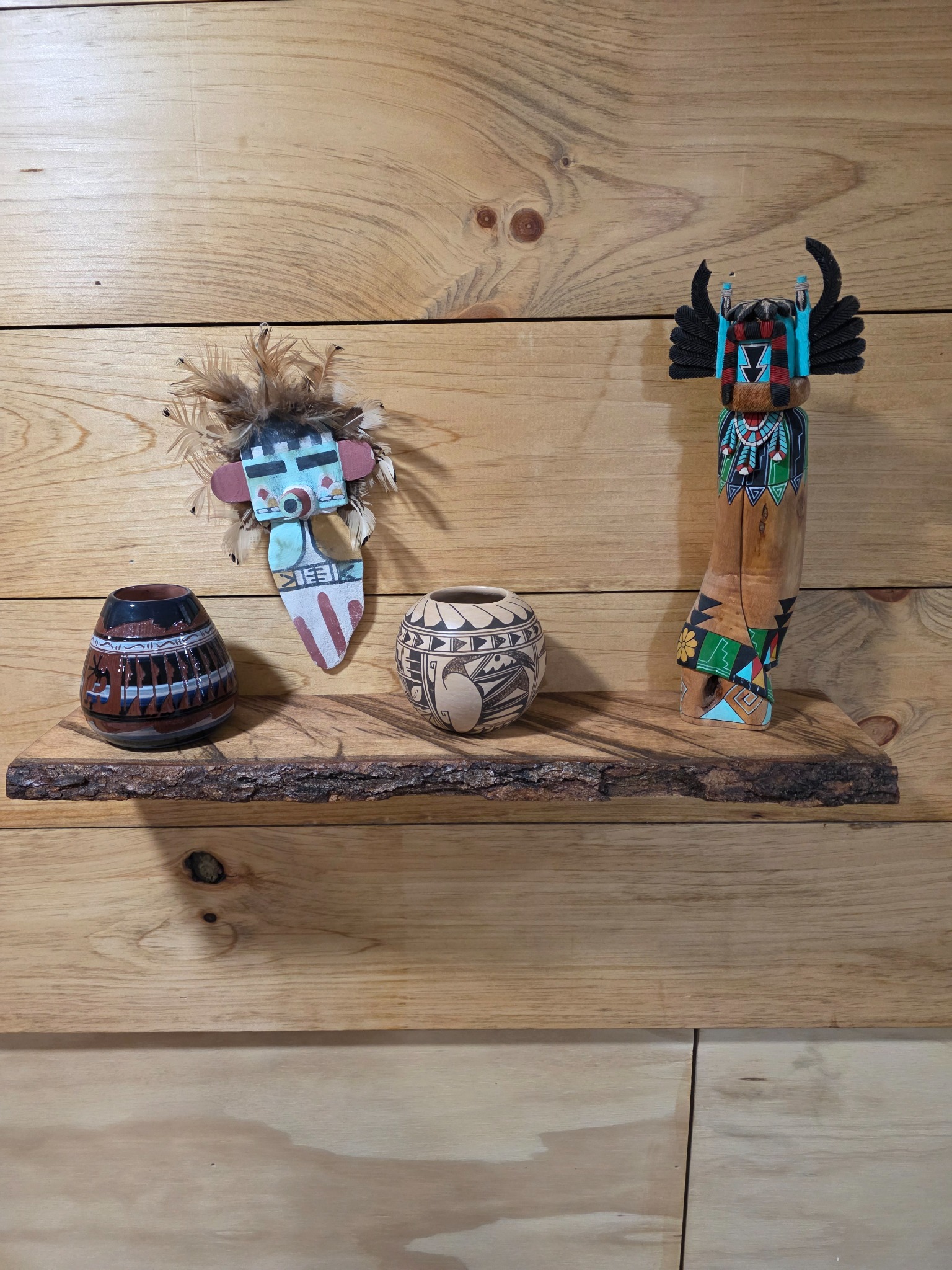 Two small pottery vessels and two katsina-style carvings on a bark-edge maple shelf